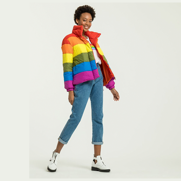 mulher usando jaqueta multicolorida com as cores da bandeira pride, camiseta branca e calça jeans com tênis